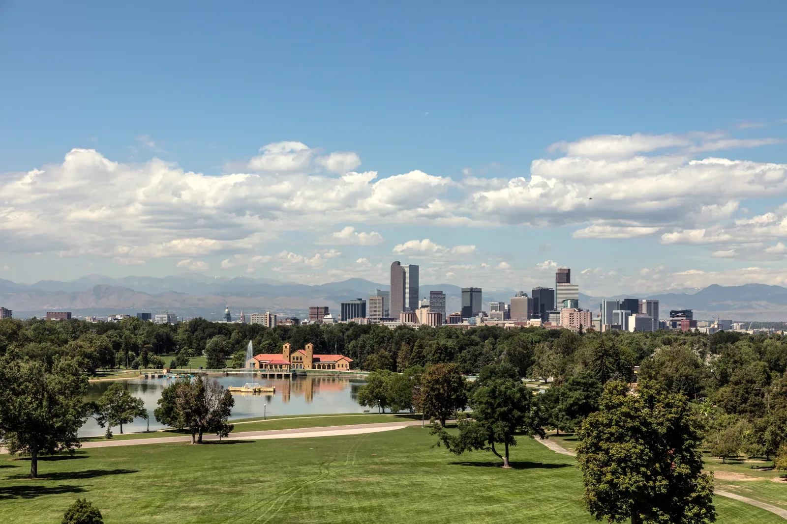 The Denver skyline across Ferril Lake in City Park, with the Front Range on the horizon under a bright sky.