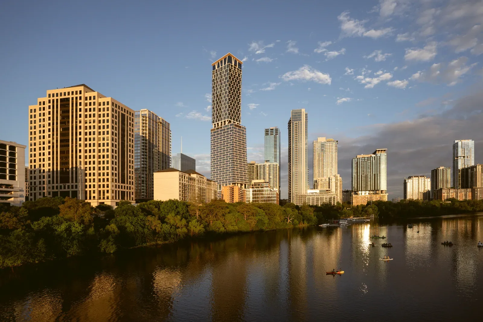 Downtown Austin's skyline in warm evening light, reflected in Lady Bird Lake, with a few kayakers on the water.